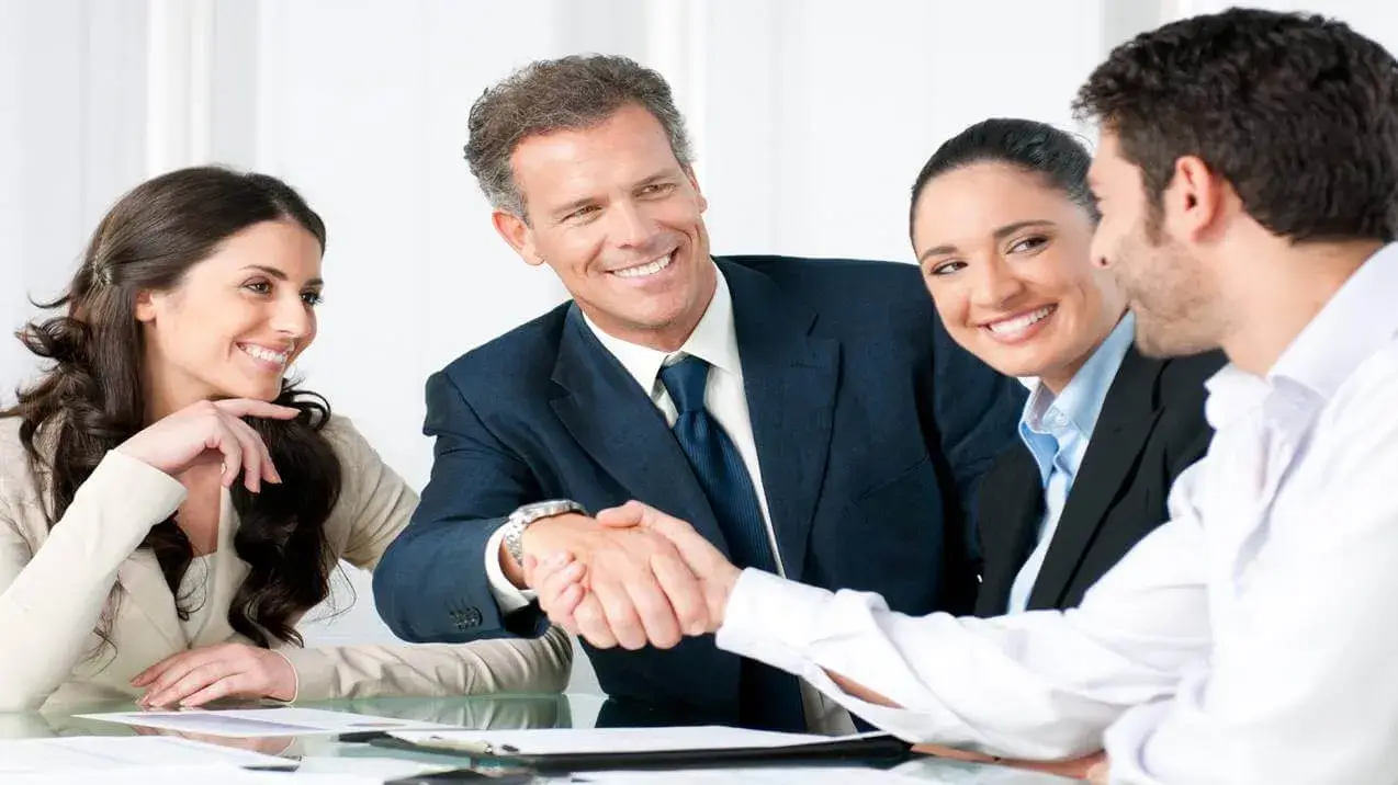 Profissionais celebram acordo com aperto de mão, um dos benefícios de dominar técnicas de vendas em uma reunião de sucesso.