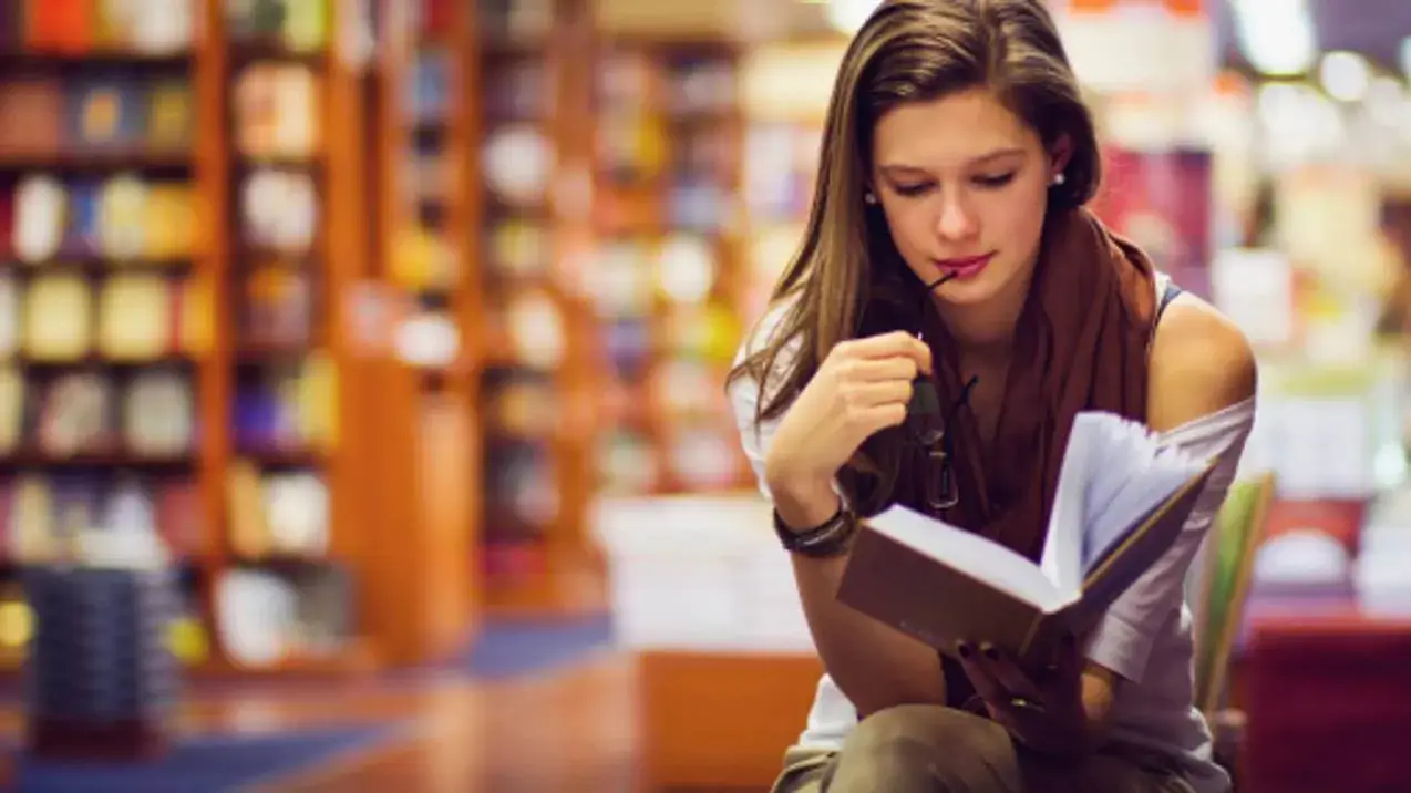 Mulher em uma livraria, concentrada na leitura de um dos Livros sobre Técnicas de Vendas em uma estante repleta de obras.