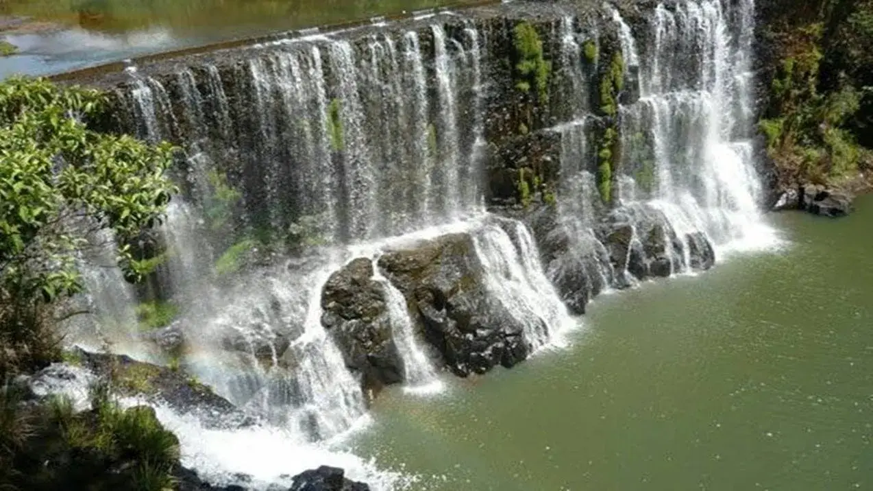 Queda d'água serena da Cachoeira do Sucupira sobre rochas com musgo, emoldurada por vegetação verde e um poço tranquilo.