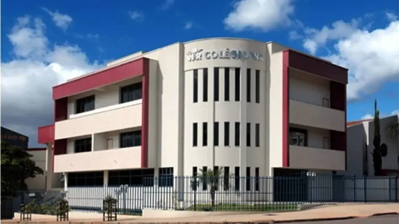 Fachada do colégio WR. Prédio moderno de três andares, branco e borgonha, em um dia de céu azul com nuvens.