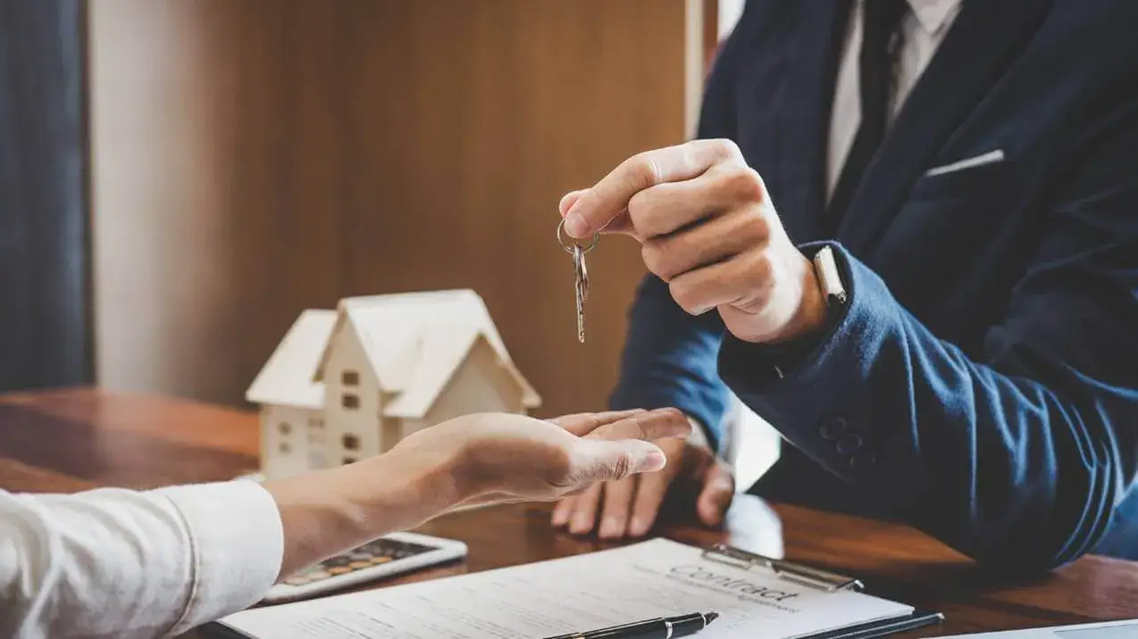 Sobre a mesa com contrato, agente entrega as chaves, mostrando como identificar uma imobiliária de confiança.