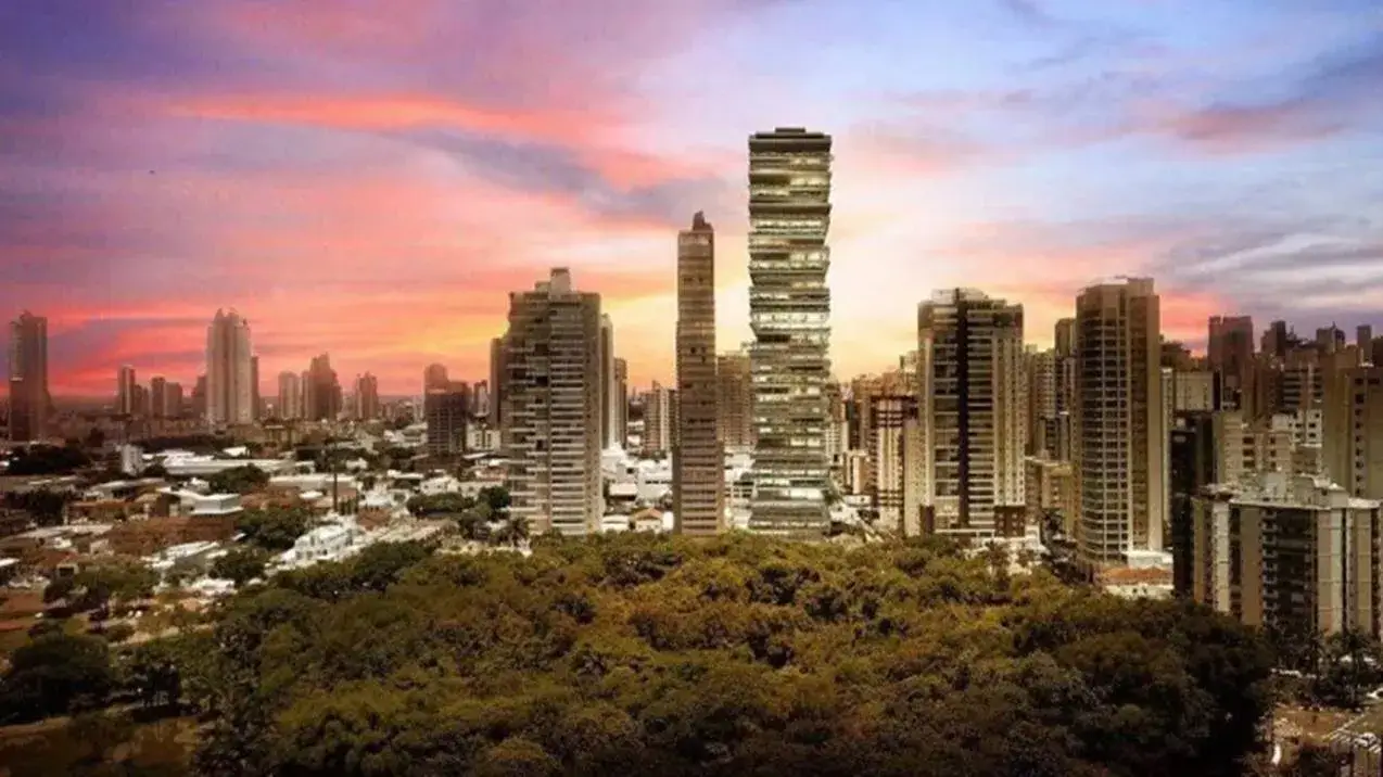 Vista de arranha-céus da epic city home Goiânia ao pôr do sol, com vegetação densa em primeiro plano e céu alaranjado.