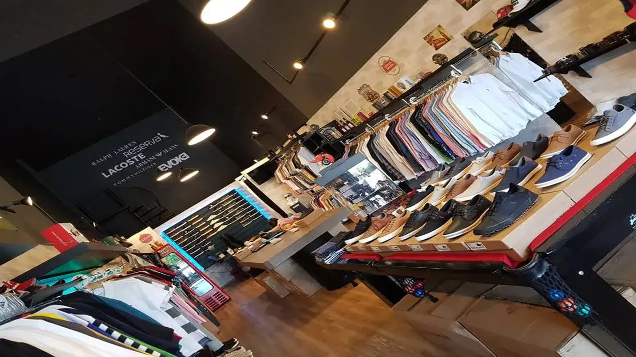 Loja de roupas moderna com teto preto e piso de madeira. Araras com peças e sapatos expostos. Uma das lojas no Jardim América.