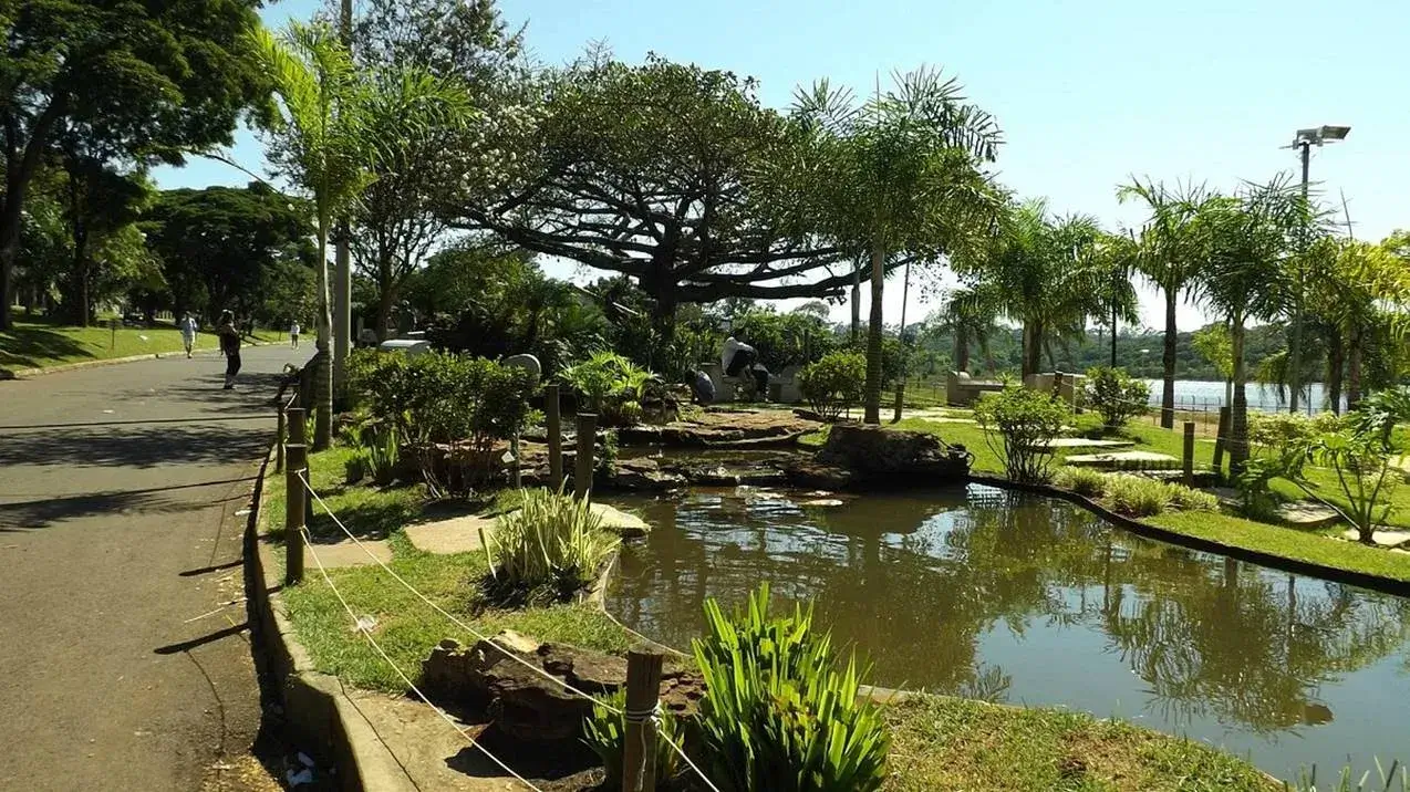 Pontos turisticos de uberlandia parque do sabia: lago com cascata, vegetação e pessoas aproveitando um dia de sol.