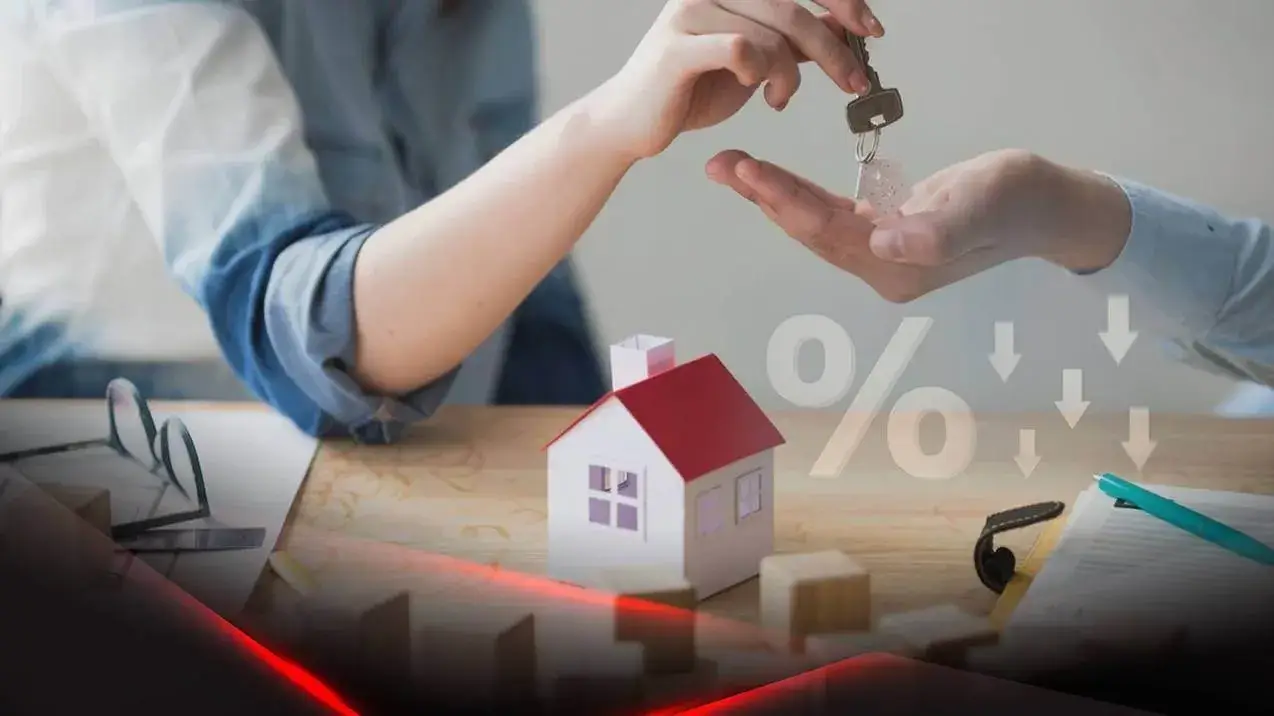 Mãos trocam chave sobre casa miniatura com símbolo de queda, indicando redução nas taxas e comissões-imobiliárias.