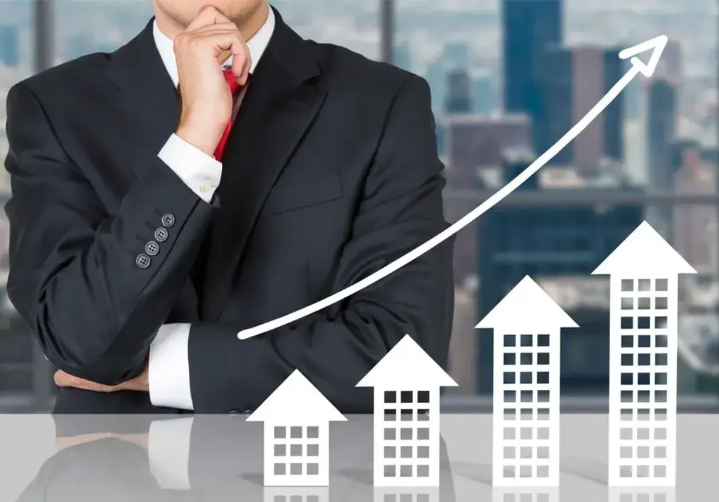 Homem de terno pensativo diante de casas e seta ascendentes, simbolizando o investimento em sua carreira e o sucesso futuro.