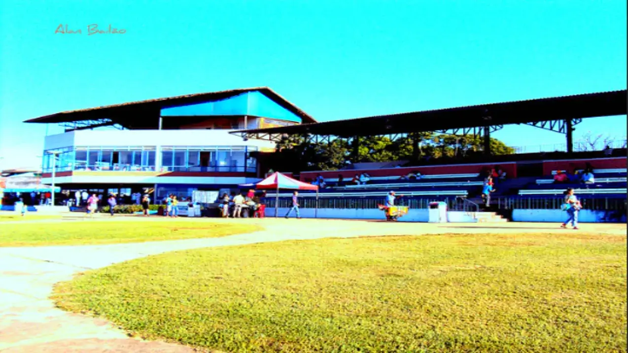 Fachada do Hipódromo da Lagoinha num dia de sol, com a arquibancada, o prédio principal e um gramado em primeiro plano.