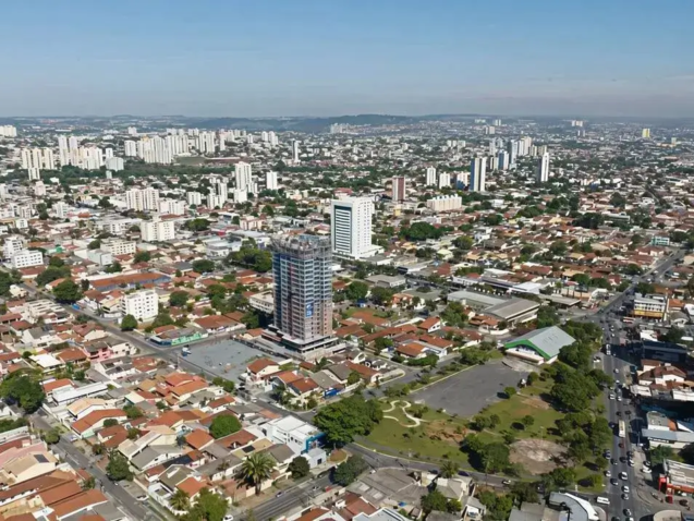 Vista aérea de Jardim América, Goiânia. Casas baixas e arborizadas contrastam com prédios altos sob um céu azul e ensolarado.