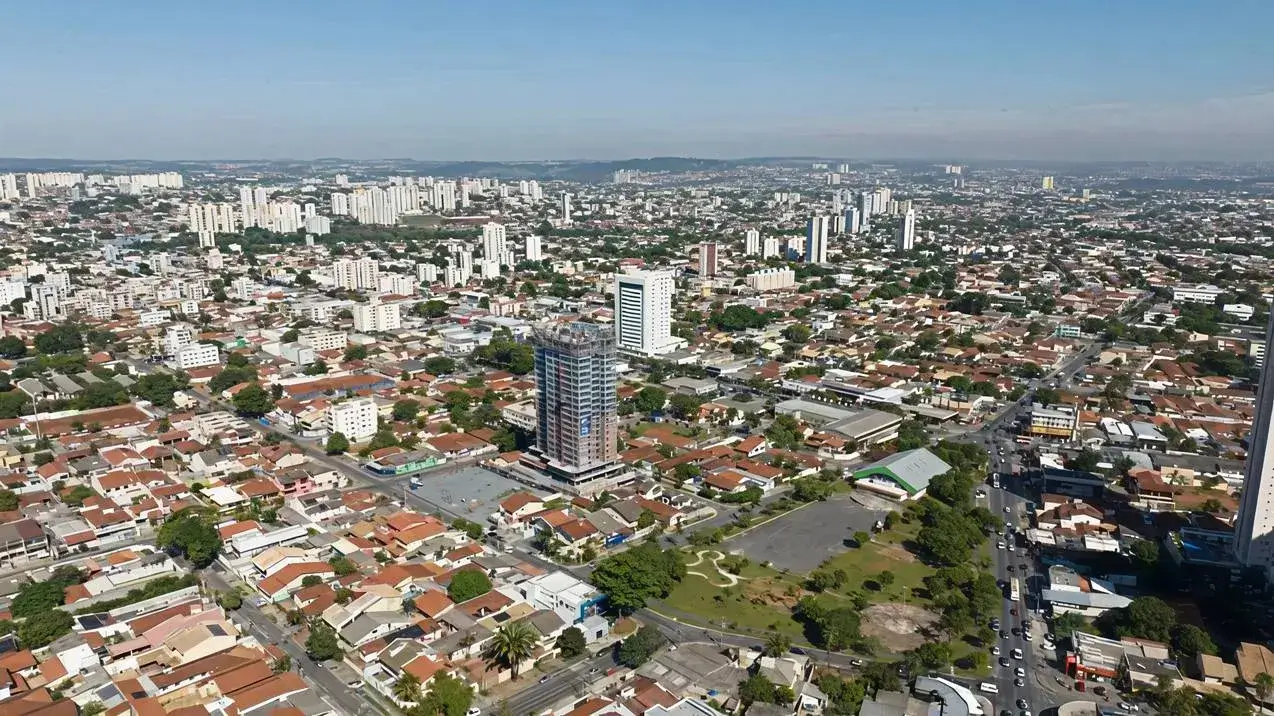 Vista aérea de Jardim América, Goiânia. Casas baixas e arborizadas contrastam com prédios altos sob um céu azul e ensolarado.