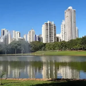 Parque no Setor Bueno com lago espelhado, refletindo prédios modernos e vegetação sob um céu azul.