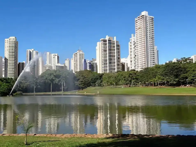 Parque no Setor Bueno com lago espelhado, refletindo prédios modernos e vegetação sob um céu azul.