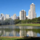 Parque no Setor Bueno com lago espelhado, refletindo prédios modernos e vegetação sob um céu azul.