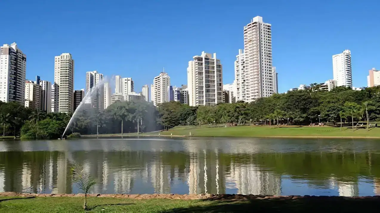 Parque no Setor Bueno com lago espelhado, refletindo prédios modernos e vegetação sob um céu azul.